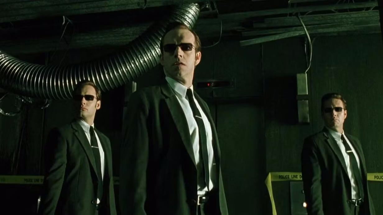 Three suited figures with sunglasses in a green-lit industrial corridor, Matrix style.